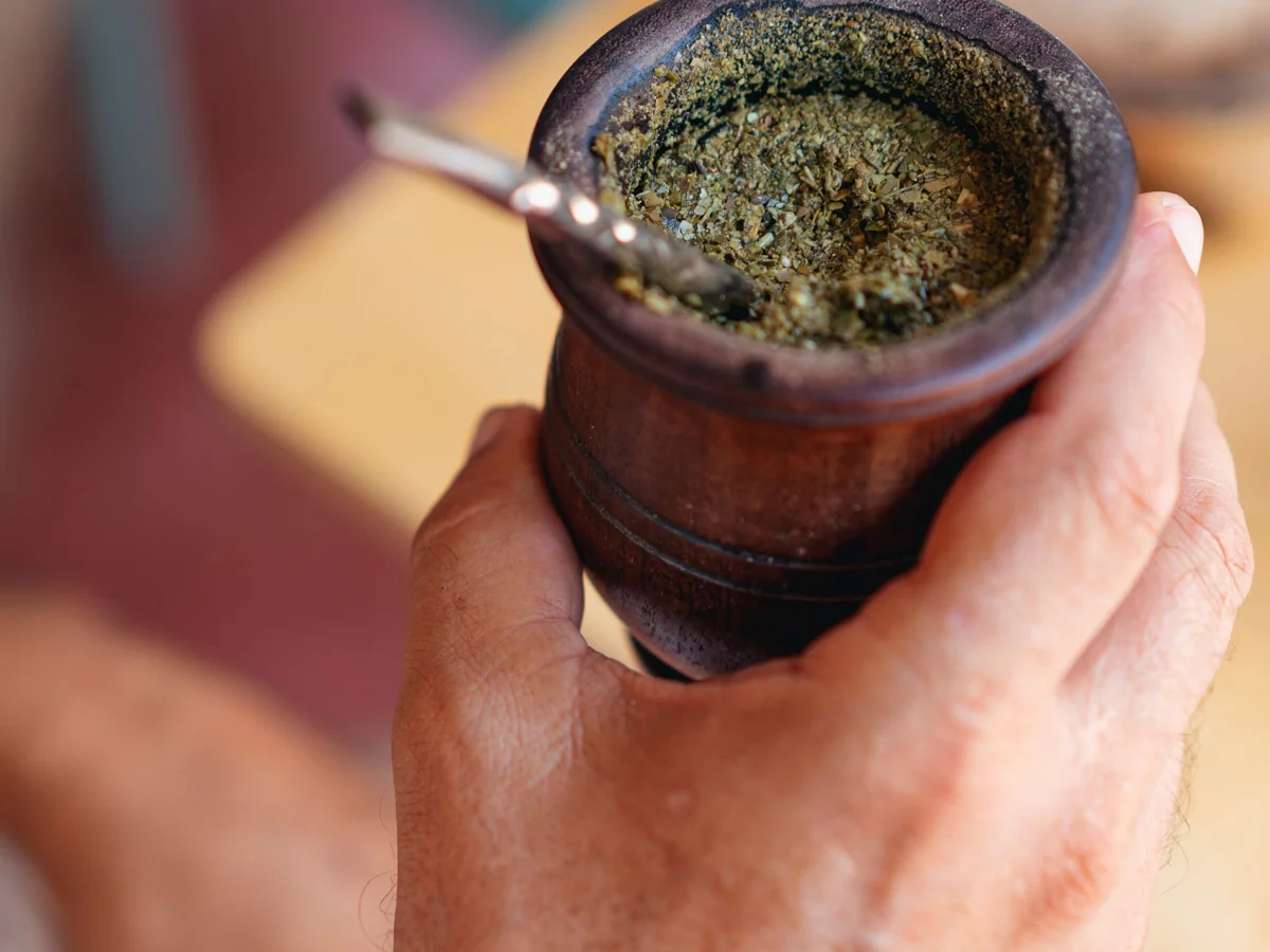 Una mano sostiene un mate de madera, junto a una mesa